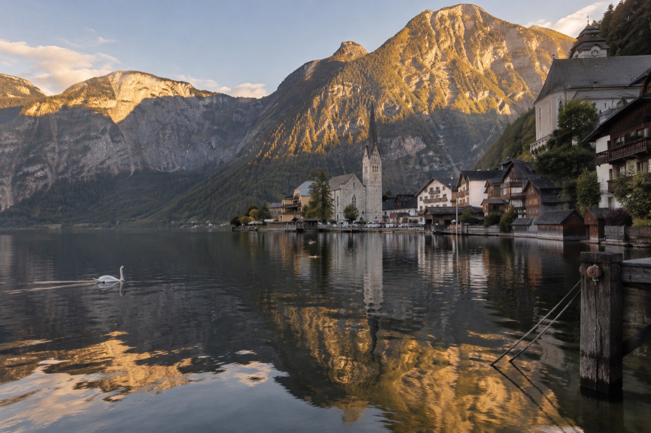 Alpine village church with mountains rising behind a lake at golden hour
