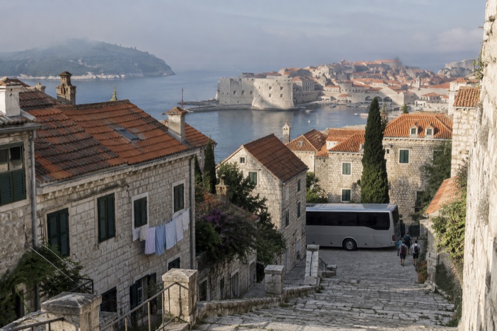 A touring coach parked on a cobbled European street lined with old stone buildings