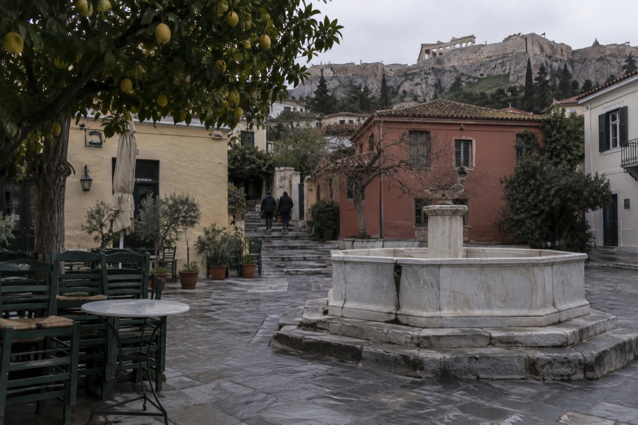 Empty cobblestone square in a European old town with cafe tables and a stone fountain