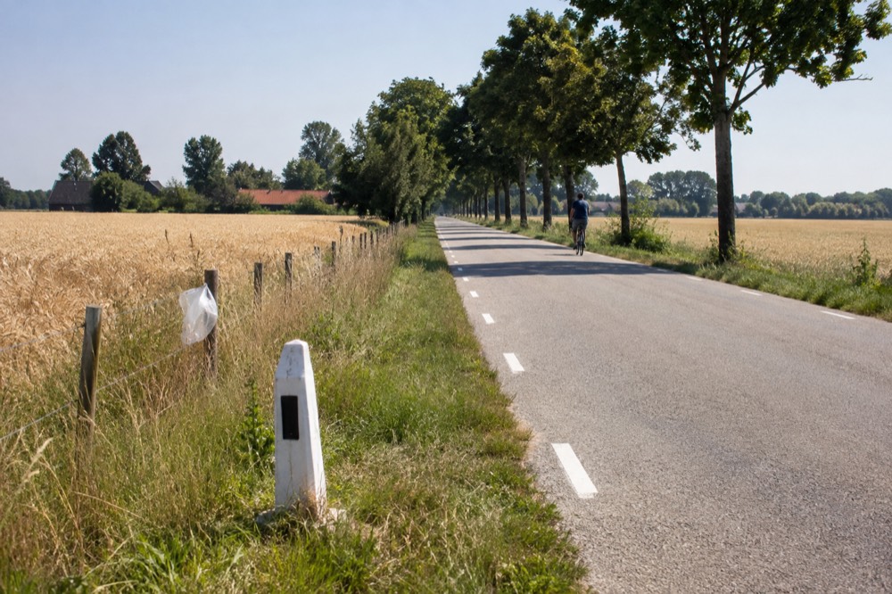 A border crossing road sign between two European countries with farmland on both sides