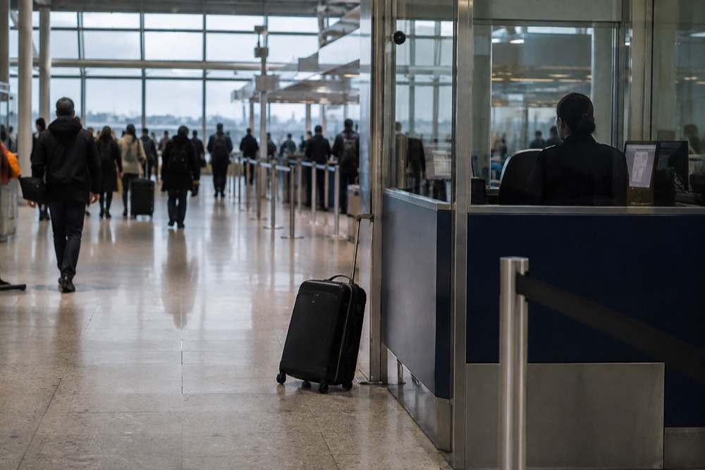 A border control booth at a modern European airport terminal with queues of travellers