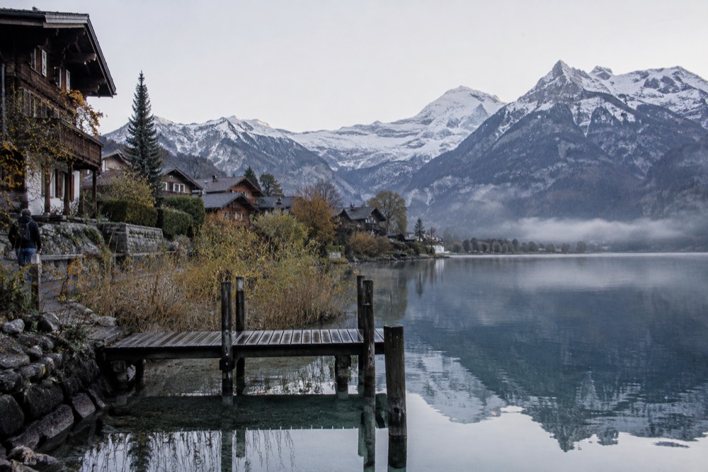 Alpine lake town with wooden chalets and mountain peaks reflected in still water