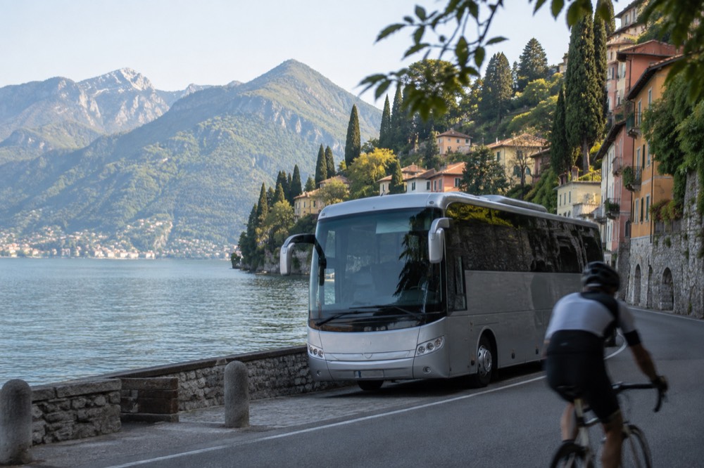 A touring coach on a road beside a lake with alpine peaks behind it