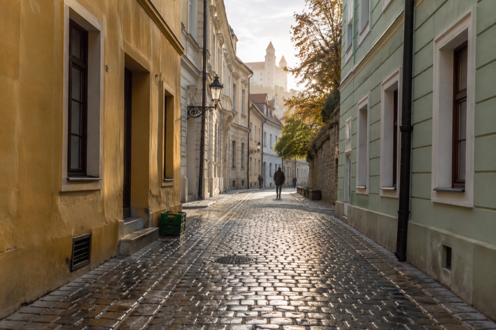 A narrow European street with pastel buildings and empty morning sidewalks
