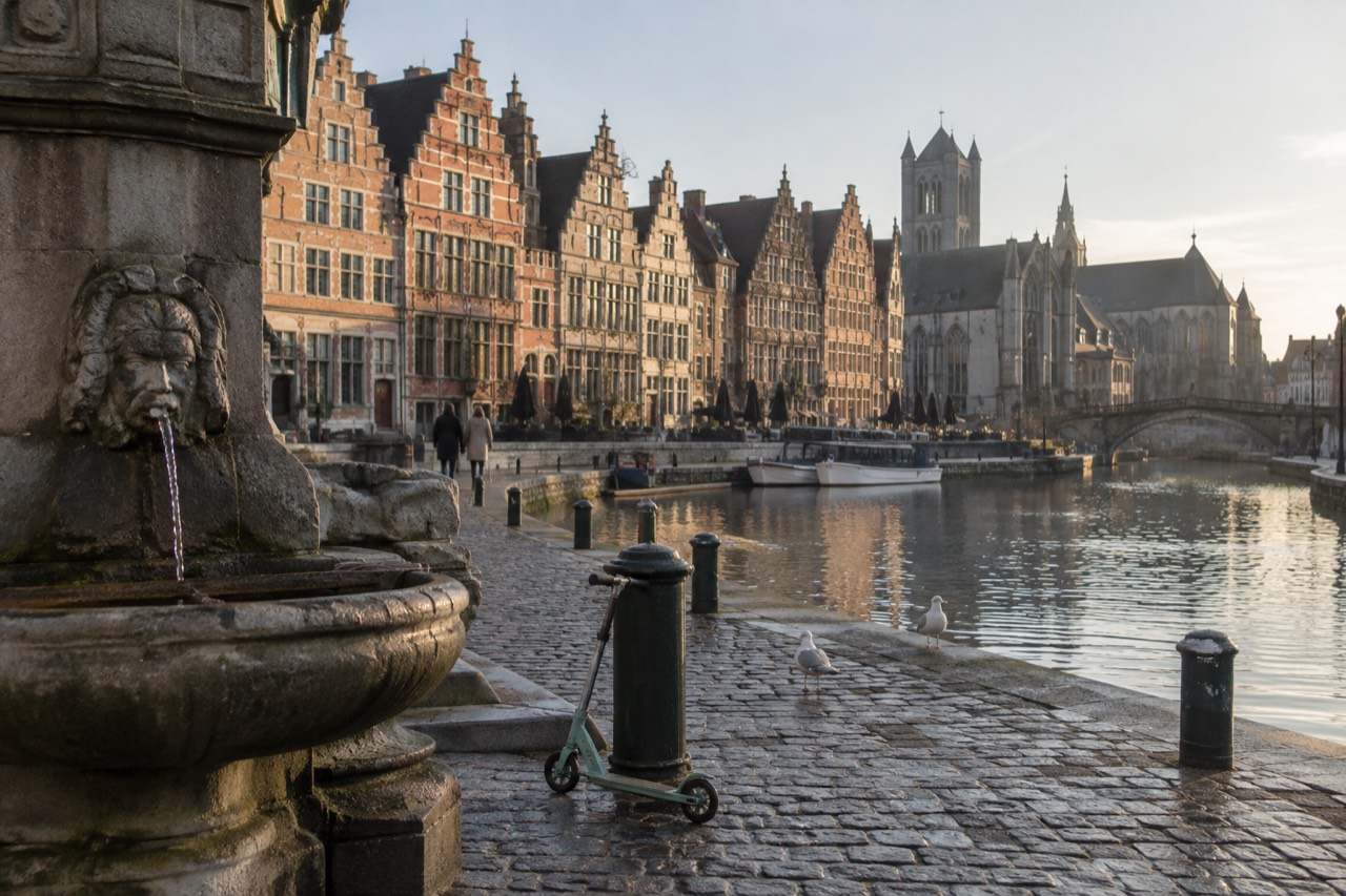 A wide European plaza with a fountain and pastel buildings in morning light