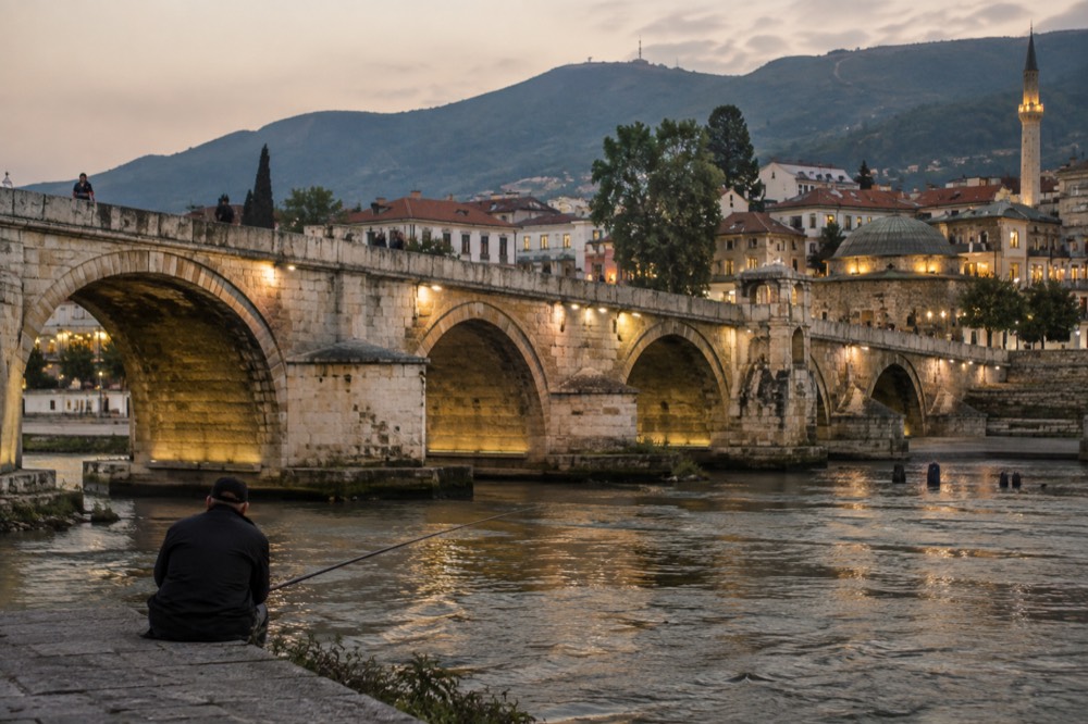 A stone bridge over a river between old town buildings in a Balkan city