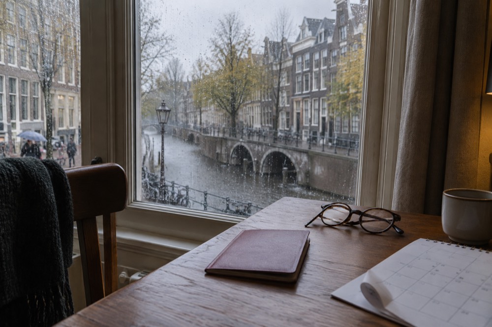 A British passport lying closed next to a calendar and reading glasses on a desk