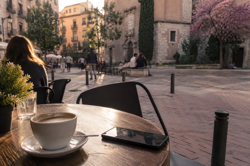 A traveller reading policy documents on a phone at a cafe table with a coffee