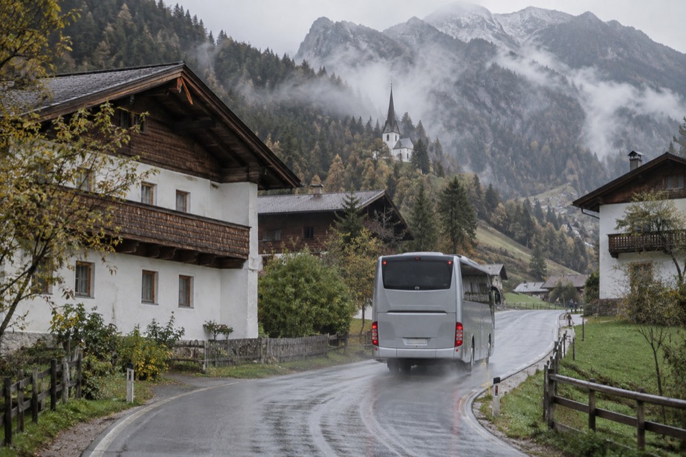 A touring coach driving on a road between alpine villages